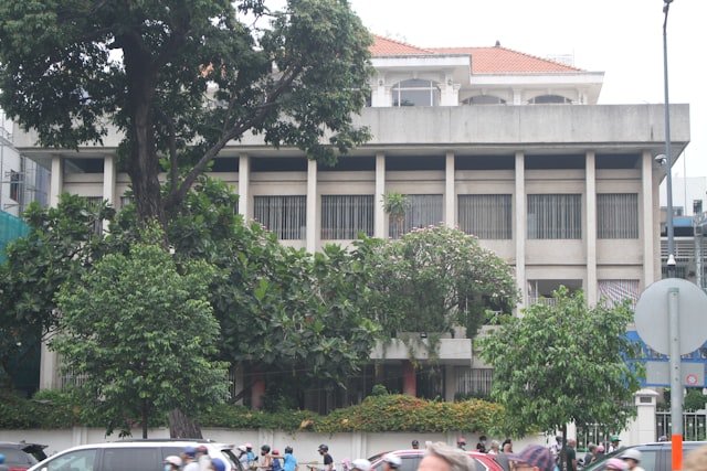 A beige building is shown with dense green foliage.